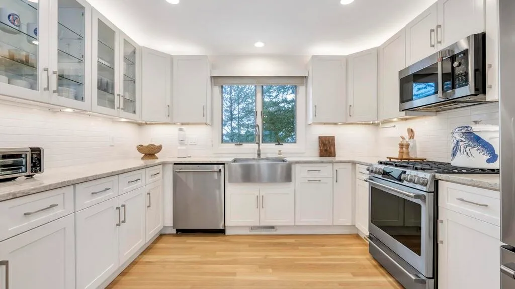 A bright kitchen with white cabinets, stainless steel appliances, and a window.