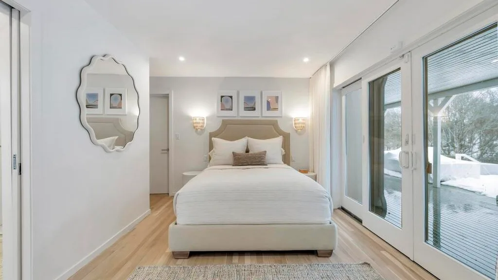 A bright bedroom with a neatly made bed and large windows.