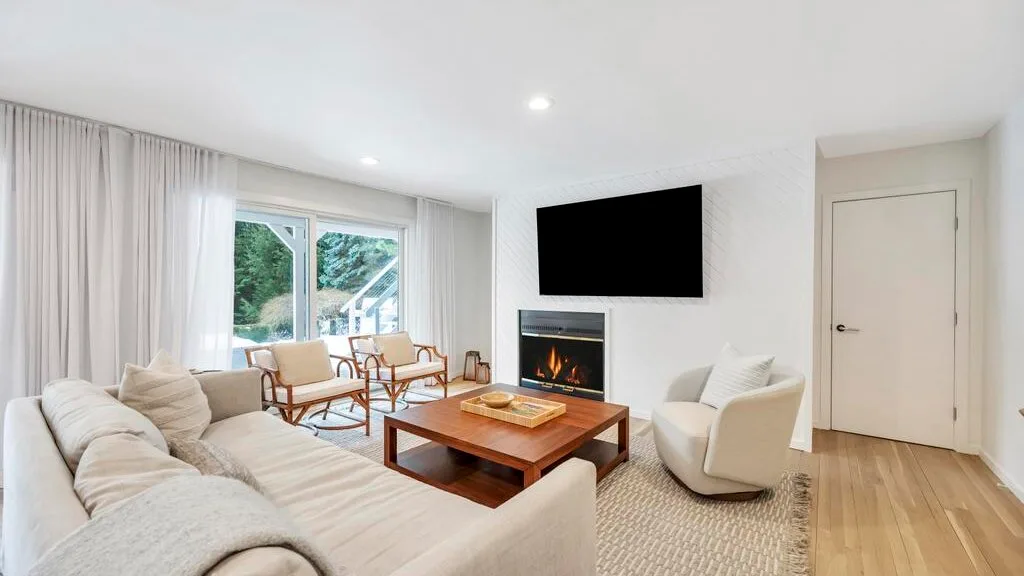 A bright living room with seating around a wooden coffee table and fireplace.