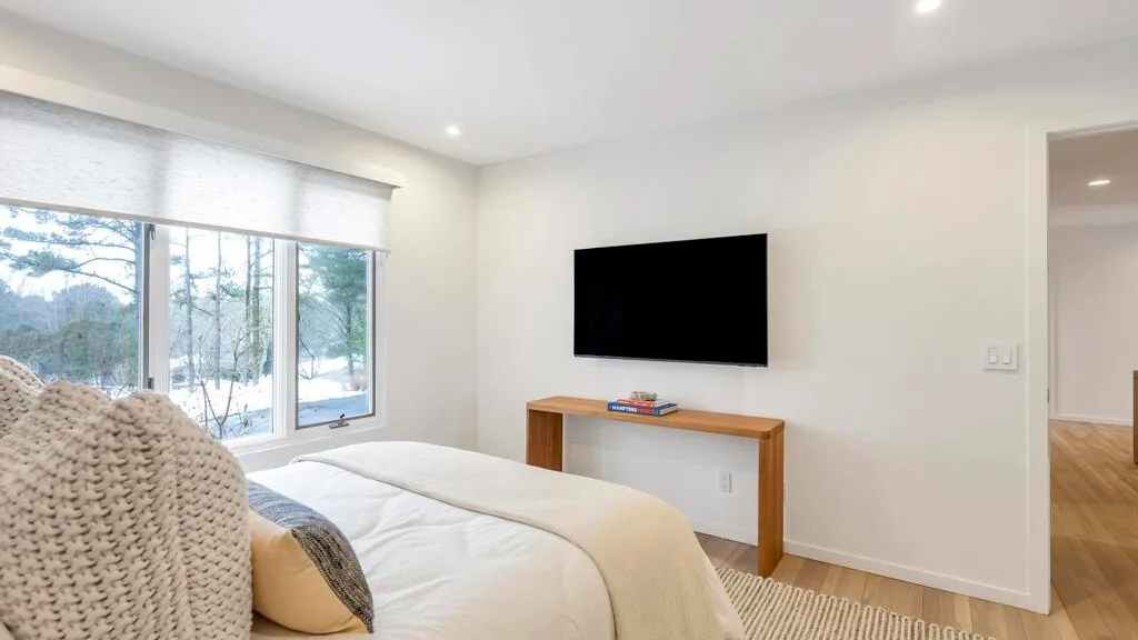 A bright bedroom with a bed, large windows, and a wall-mounted television.