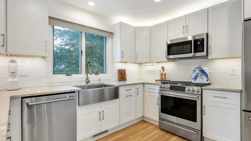A bright kitchen with white cabinetry, a stainless-steel sink, and a range.