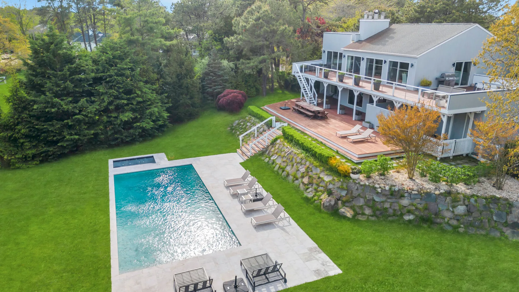 A landscaped backyard with a swimming pool beside a multi-level house and deck.