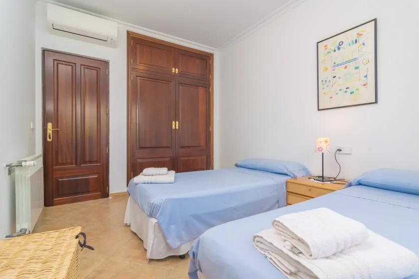 A bedroom with two beds dressed in blue bedding and wooden wardrobes.