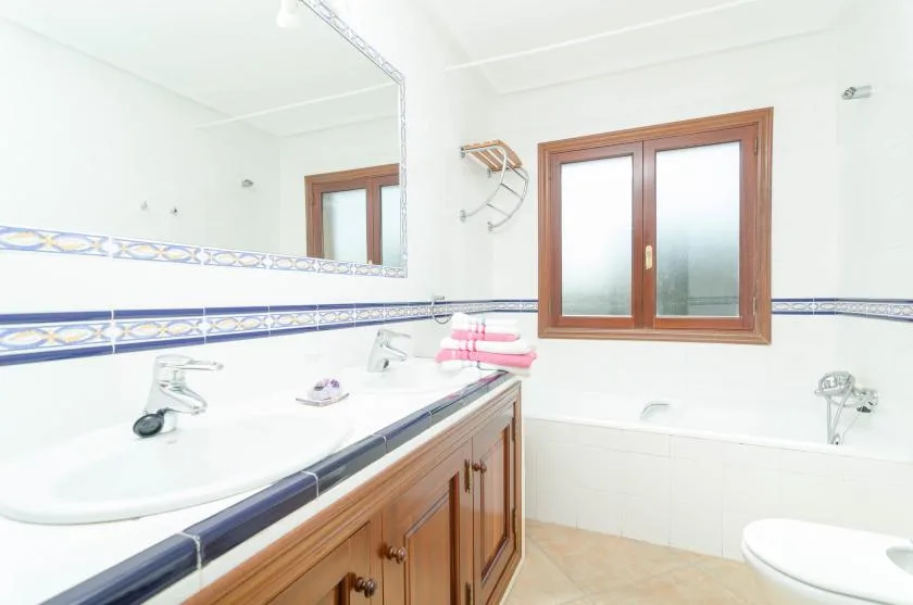 A bright bathroom with a long vanity, wall mirror, and frosted window.
