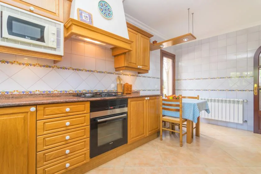 A tiled kitchen with wooden cabinets, an oven, and a small dining table.