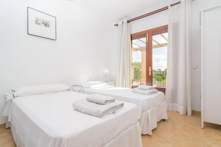 A bright bedroom with two beds beside a glass door opening onto a balcony.