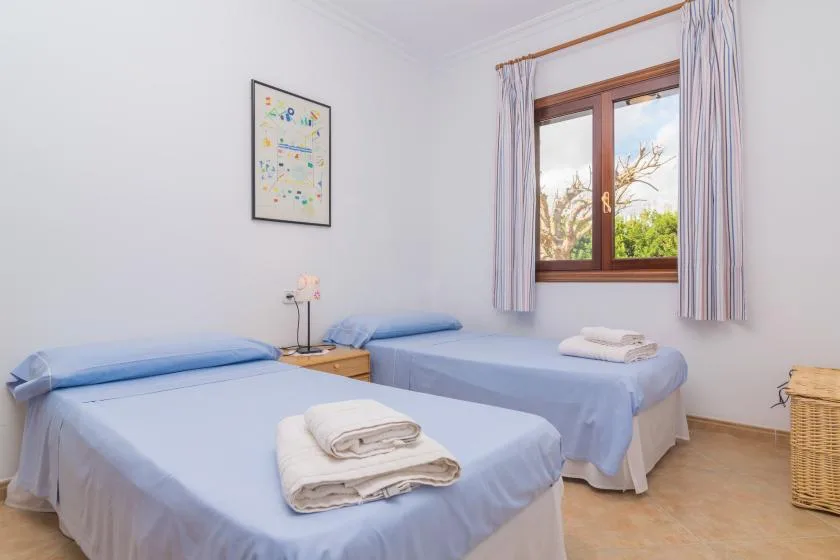 A bedroom with two beds and folded towels beside a window.