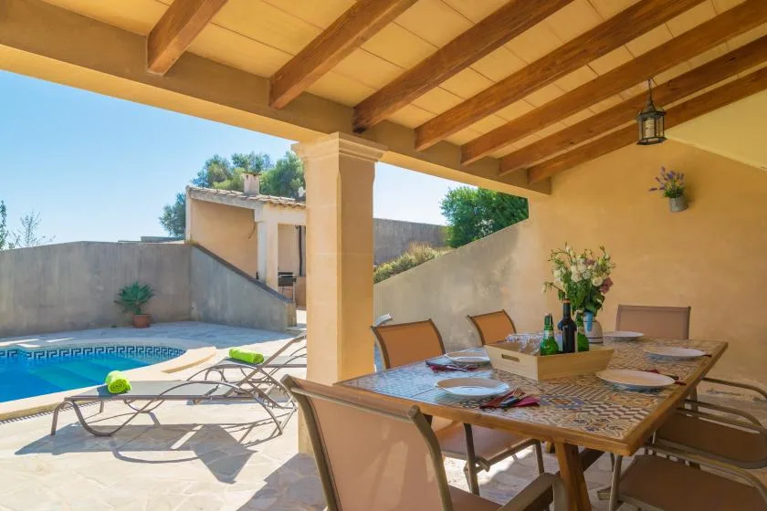A covered outdoor dining area beside a swimming pool, with a table and chairs.