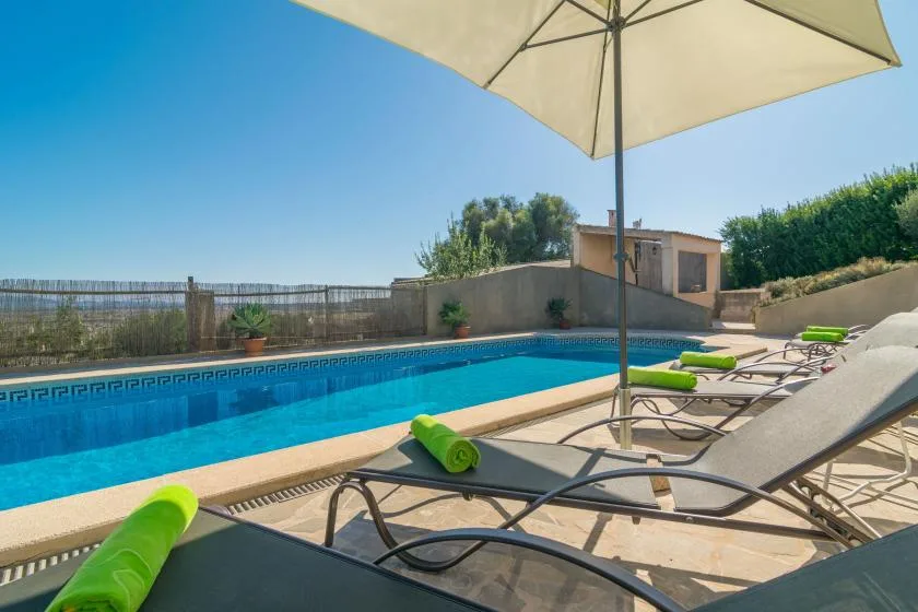 An outdoor swimming pool beside lounge chairs under a large umbrella.