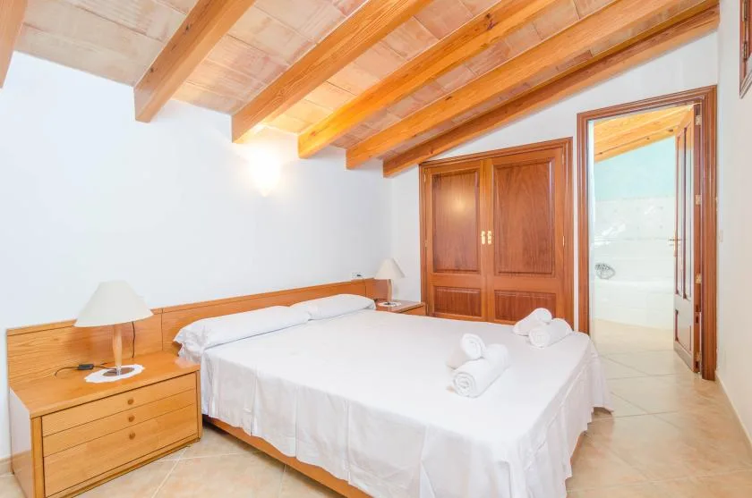 A bedroom with a large bed, wooden wardrobes, and exposed ceiling beams.