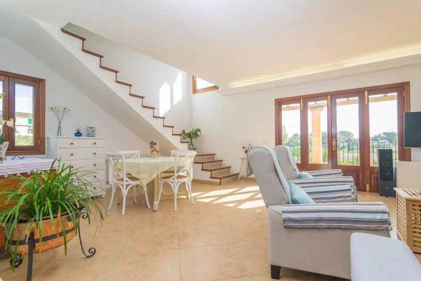 A bright living room with seating, a dining table, and a staircase.