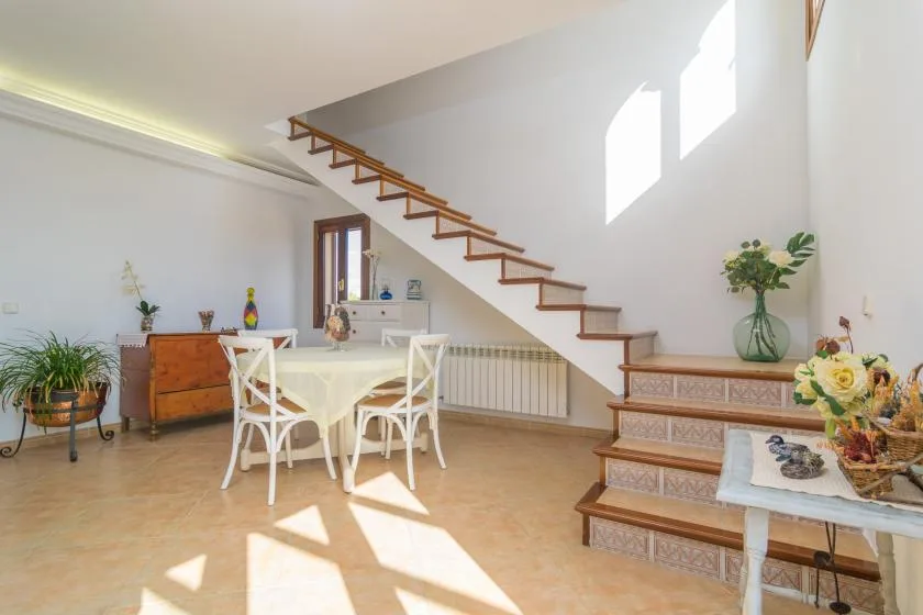 A bright dining area with a table and chairs beside a staircase.