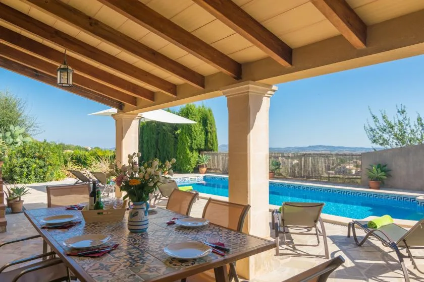 A covered outdoor dining area overlooks a swimming pool and distant hills.