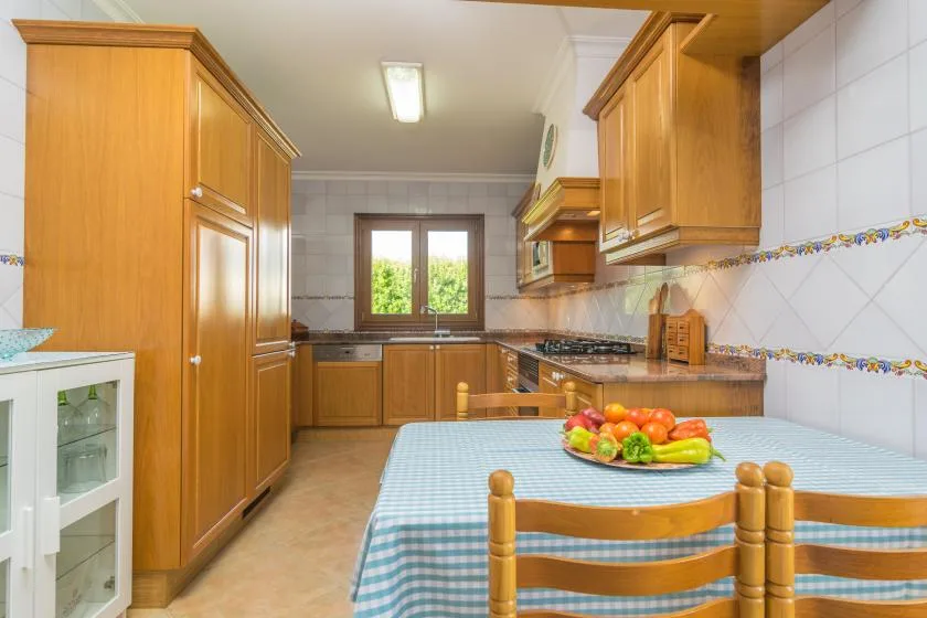 A kitchen with wooden cabinets, a window, and a checkered tablecloth.
