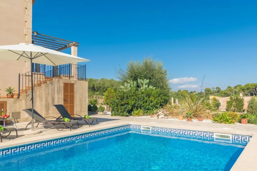 An outdoor swimming pool beside a patio with loungers and a large umbrella.