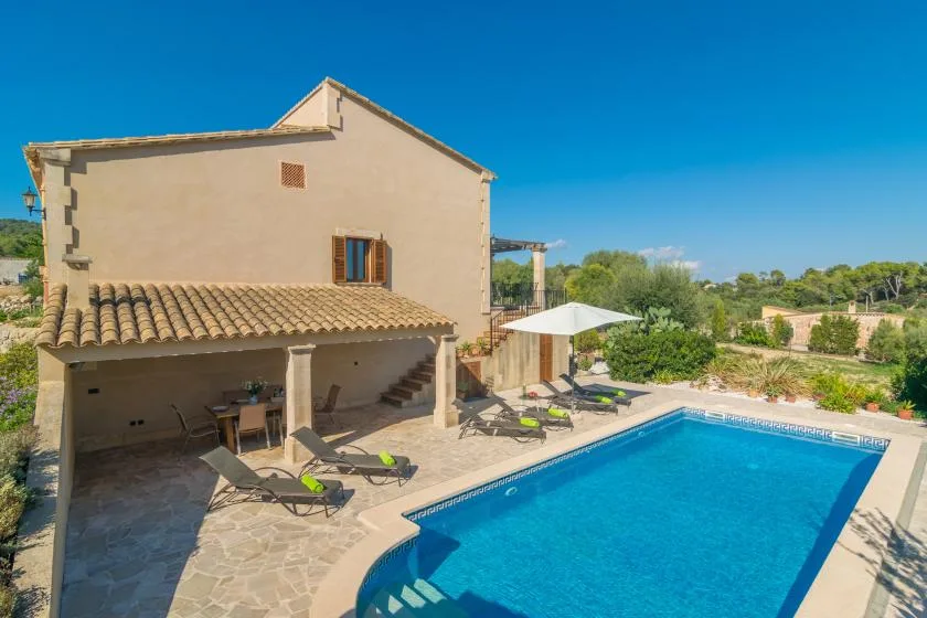 A swimming pool beside a house, with patio seating and a white umbrella.