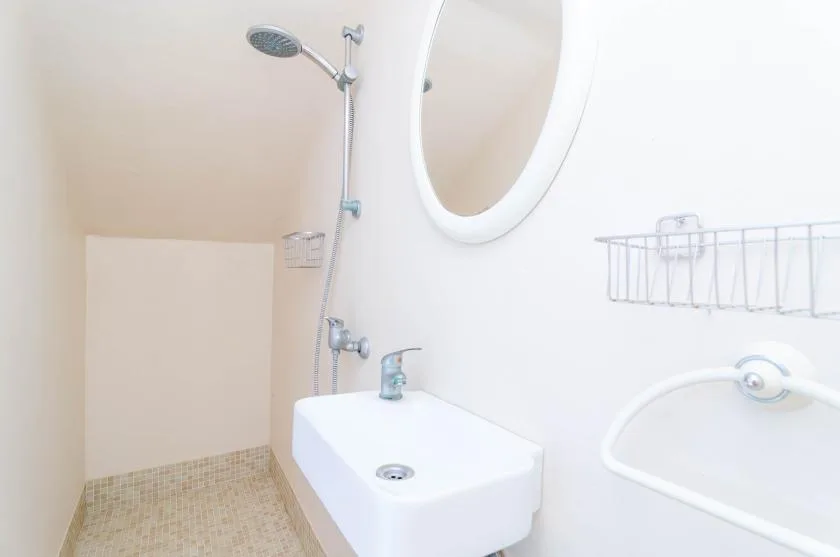 A compact bathroom with a wall-mounted sink, mirror, and shower.