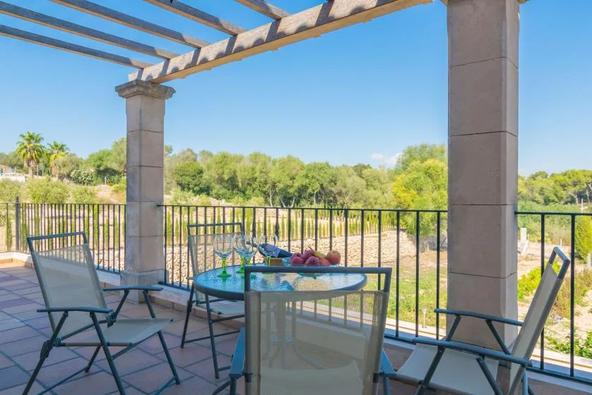 An outdoor patio seating area overlooks a green landscape beneath a pergola.