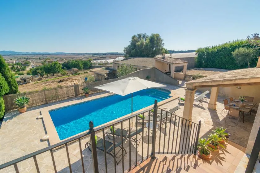 An outdoor swimming pool beside a shaded patio, with open countryside in the distance.