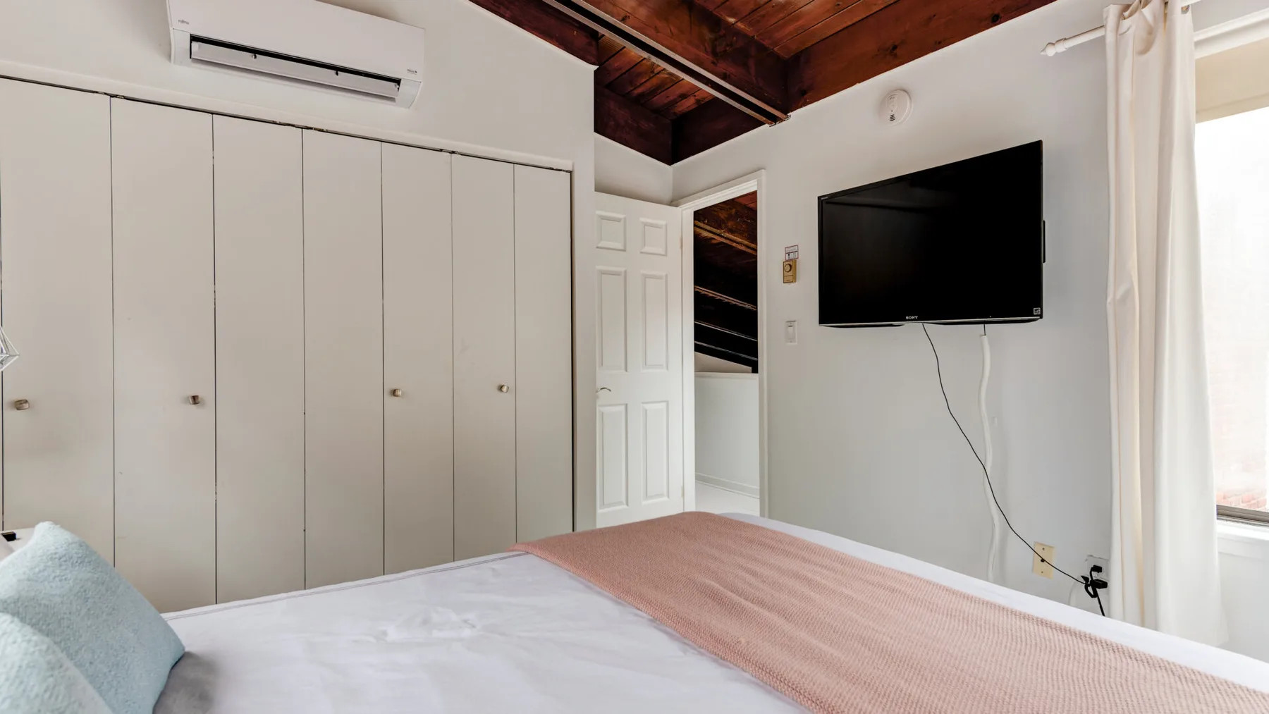 Un dormitorio con una cama, armarios empotrados y un televisor en la pared.