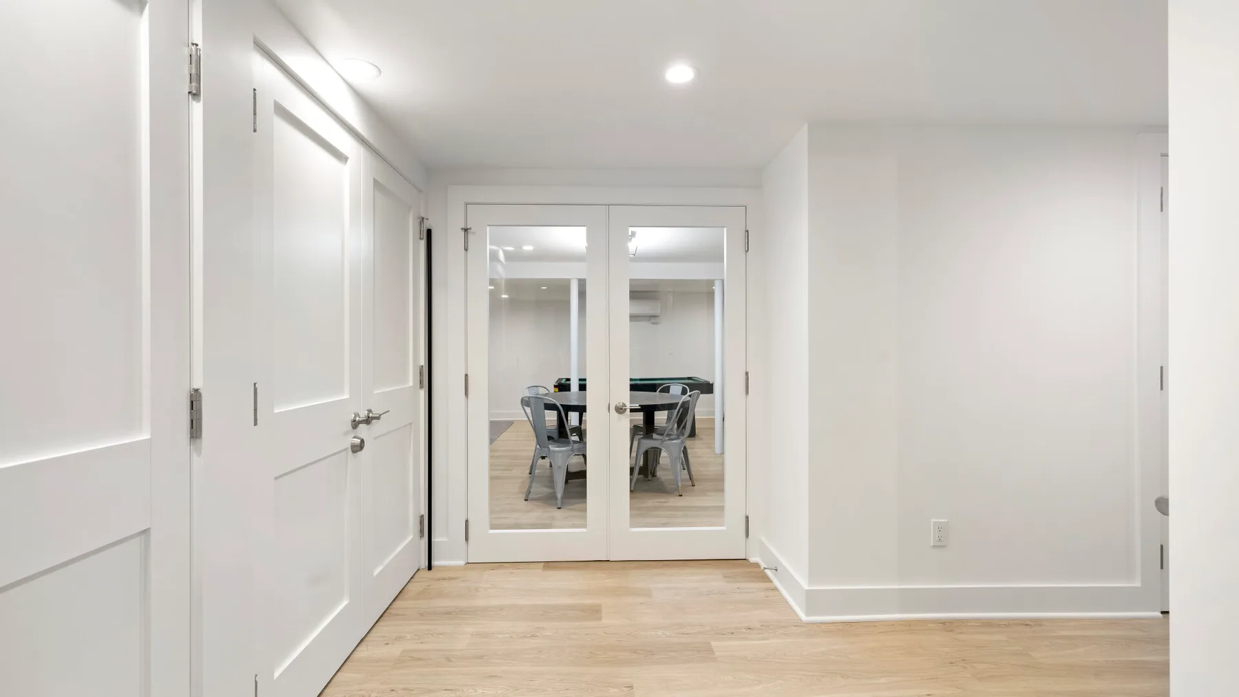 Un pasillo luminoso con puertas blancas y puertas dobles de vidrio que dan a una habitación amueblada.