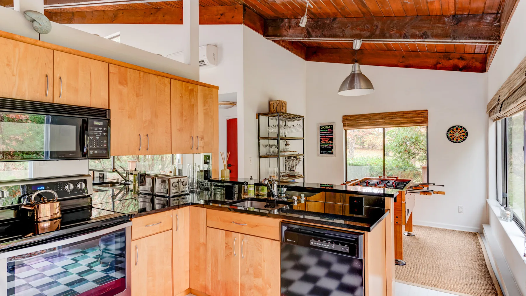 Una cocina con gabinetes de madera, encimeras negras y un techo alto revestido de madera.