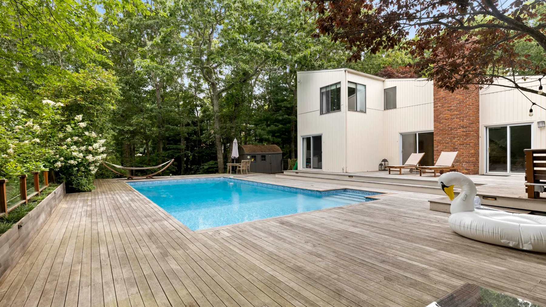 Una piscina exterior está junto a una casa moderna y una terraza de madera.