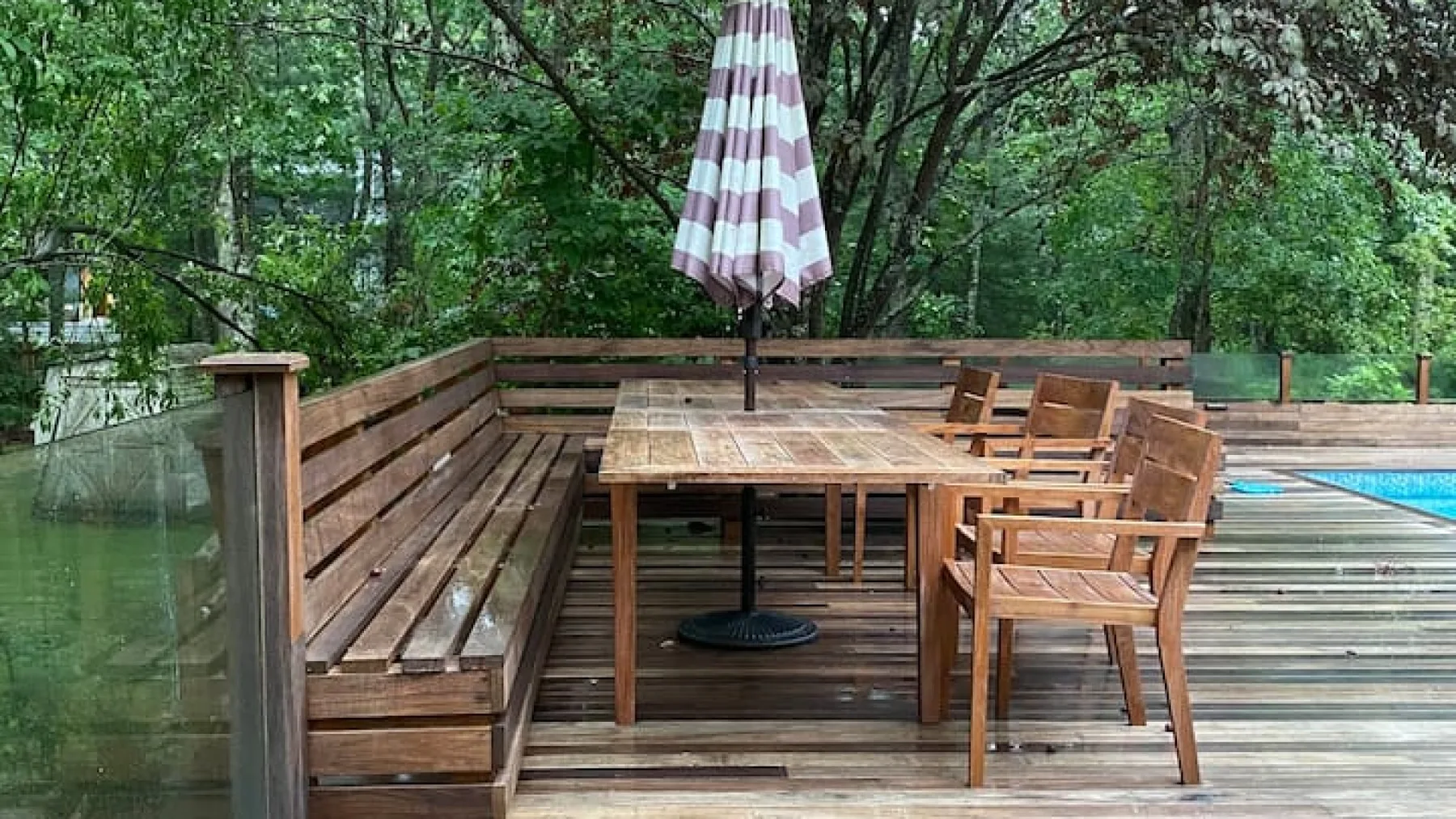 Una terraza exterior de madera tiene una mesa, asientos y una sombrilla a rayas.
