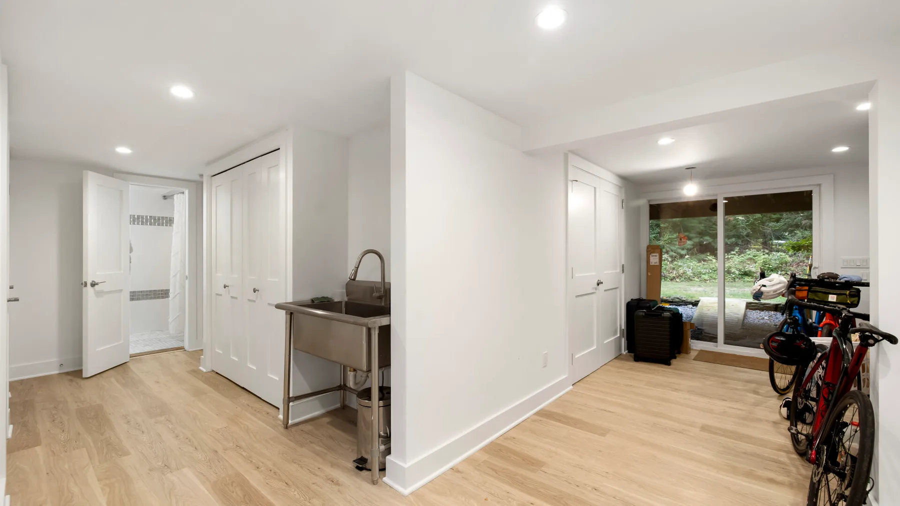 Una habitación luminosa con suelo de madera clara, un fregadero de servicio y bicicletas.