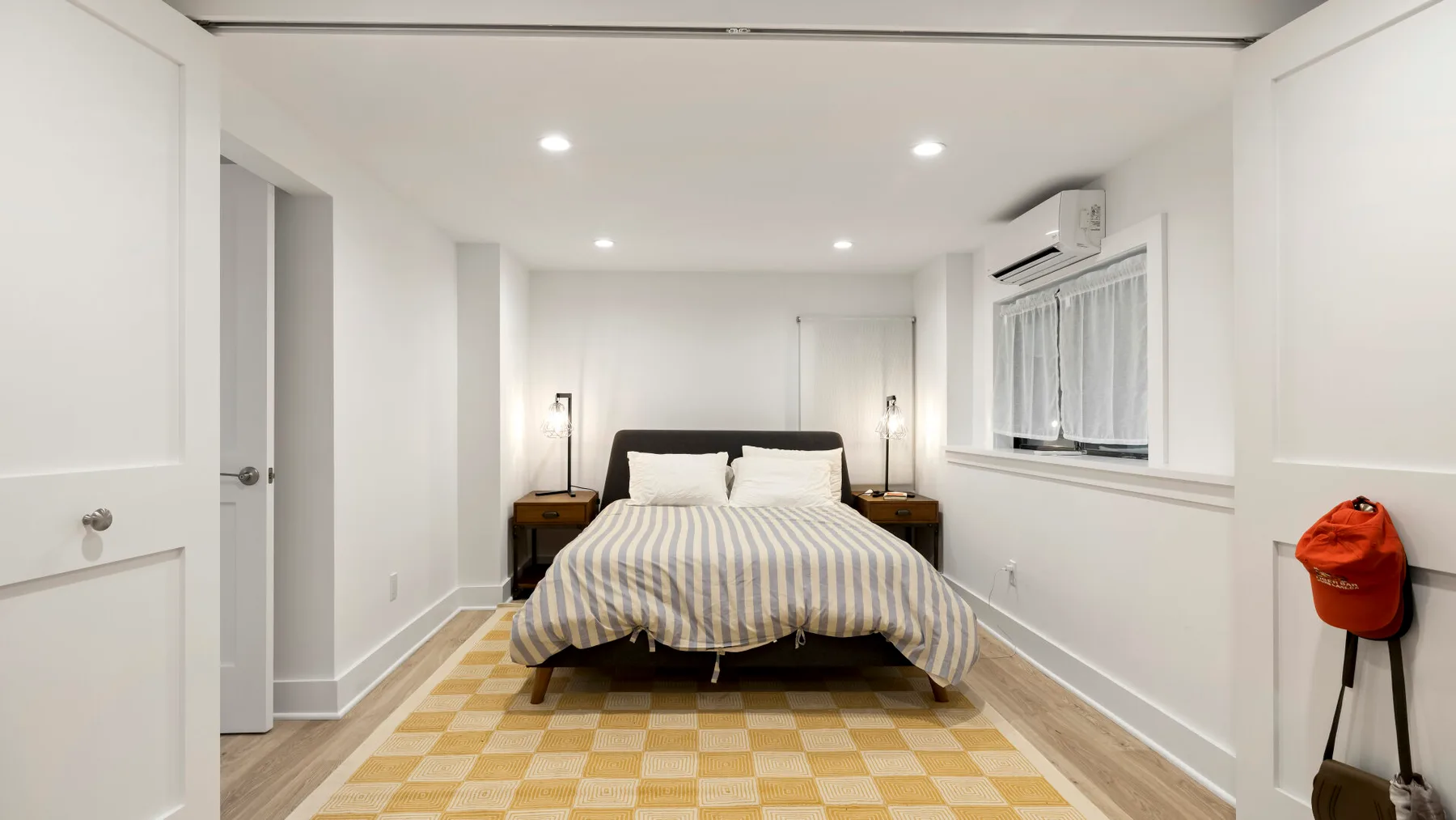 Un dormitorio con una cama bajo luces empotradas y ventanas a lo largo de la pared derecha.