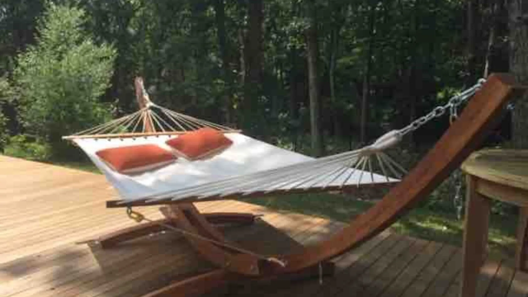 Una hamaca está sobre una terraza de madera junto a una zona arbolada.