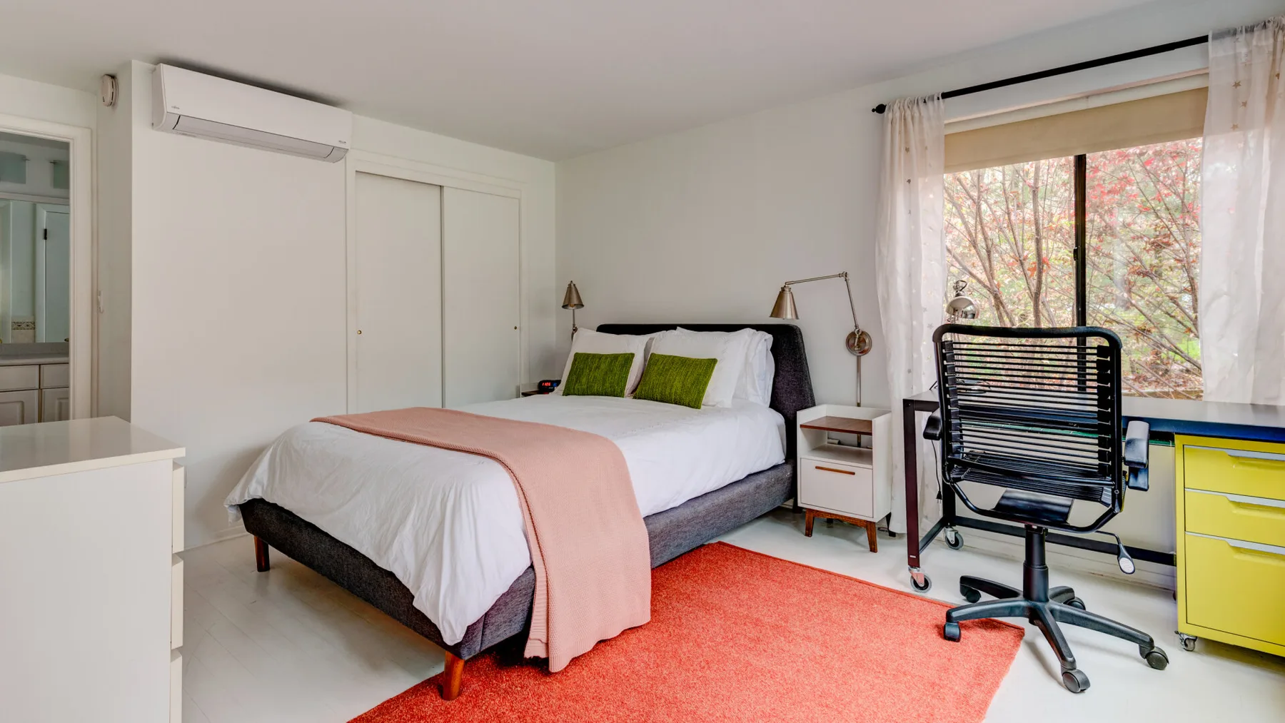 Un dormitorio luminoso con una cama, almohadas verdes y una ventana grande.