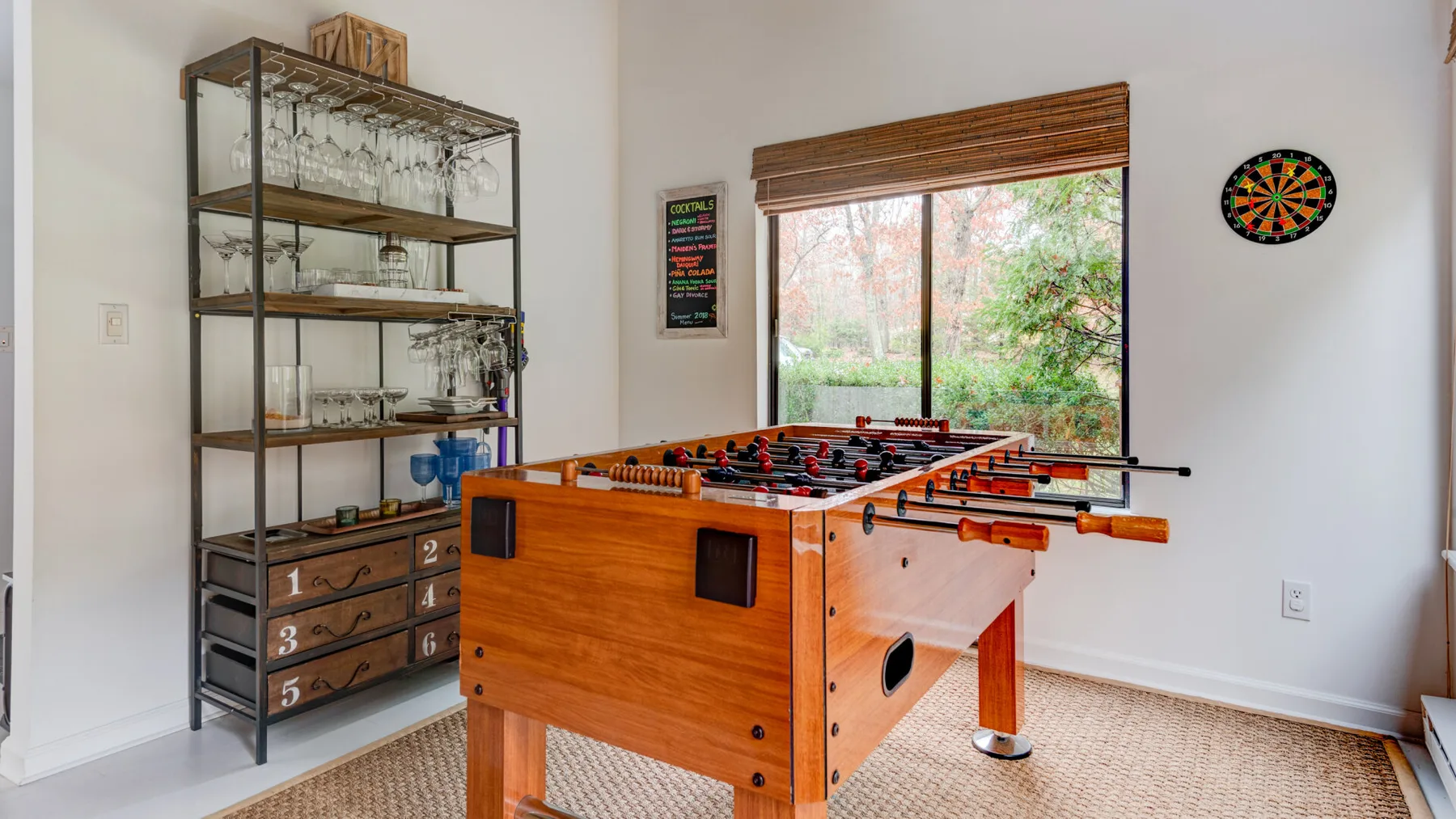 Una sala de juegos cuenta con una mesa de futbolín junto a una vitrina de cristalería.