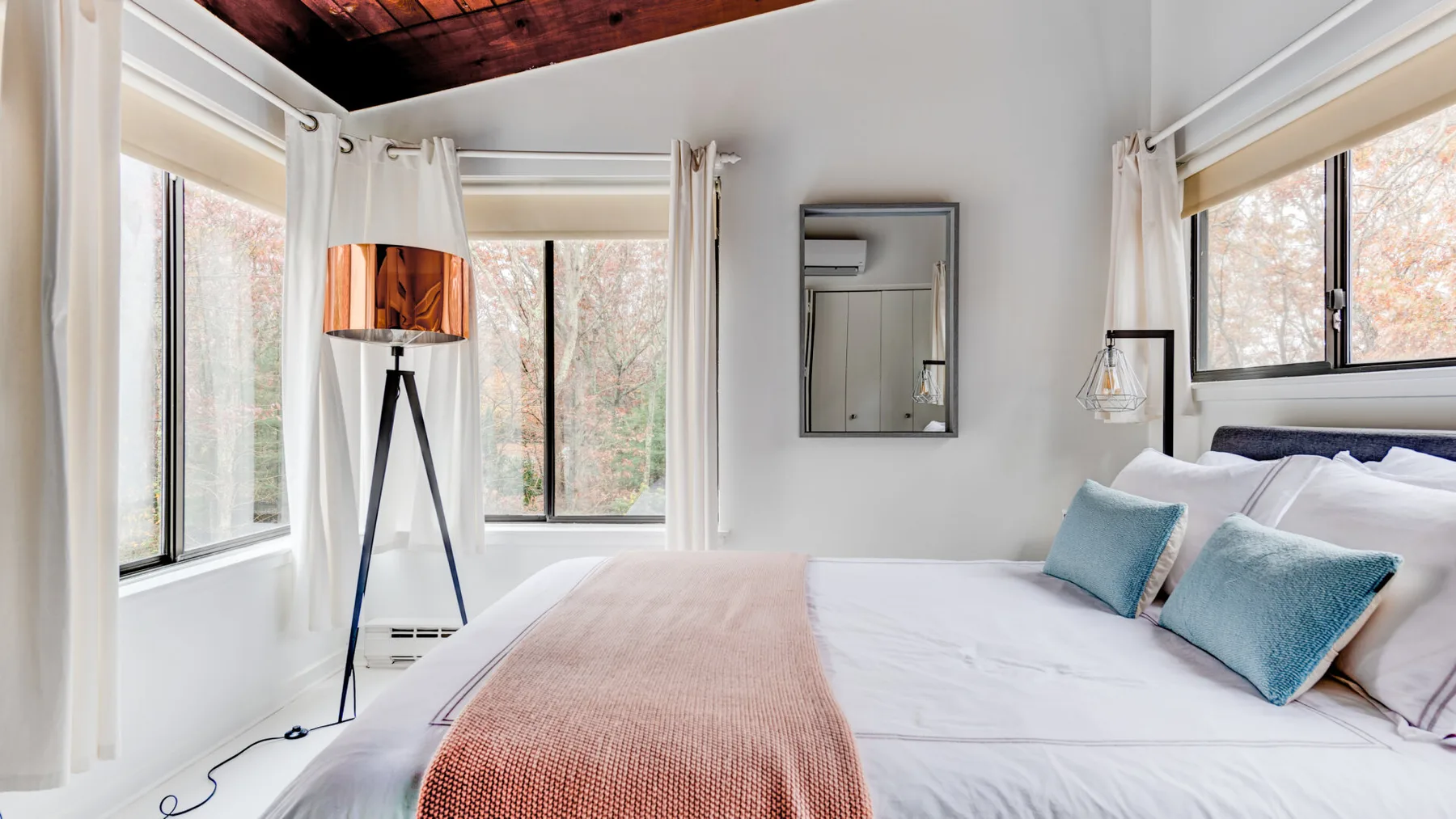 Un dormitorio luminoso con una cama bien tendida y grandes ventanas.