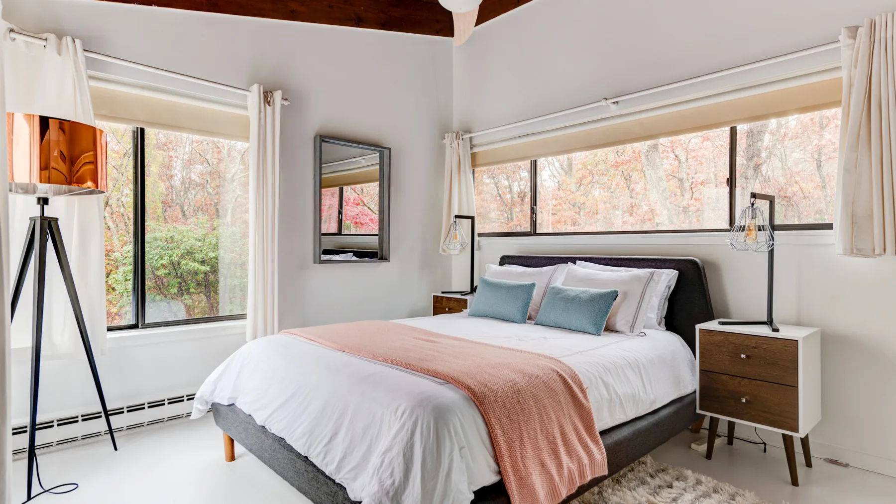 Un dormitorio luminoso con una cama tendida y grandes ventanas.