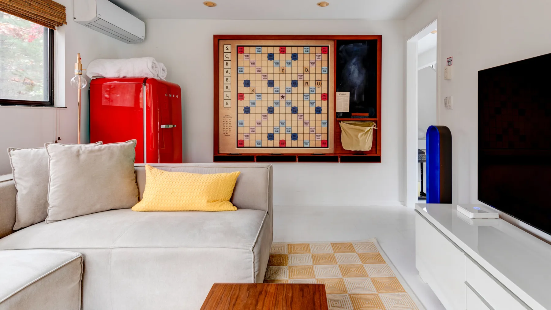 Una sala luminosa con un sofá claro y un juego de mesa montado en la pared.