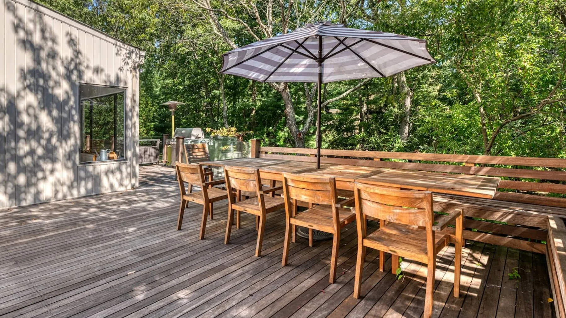 Un comedor al aire libre con una mesa larga de madera y una sombrilla grande.