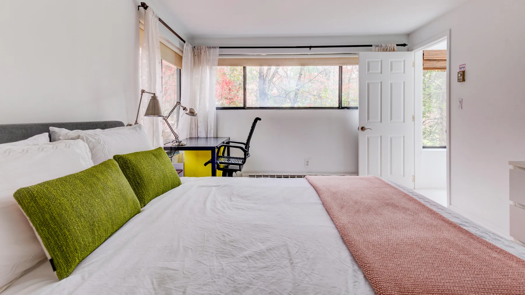 Un dormitorio luminoso con una cama grande, cojines verdes y ventanas amplias.