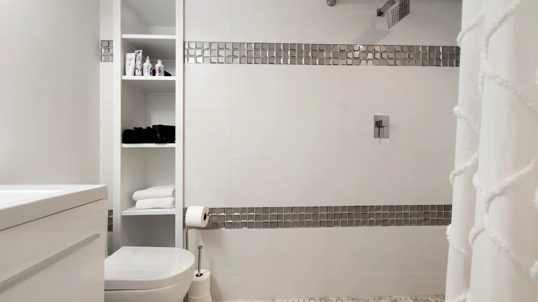 Un baño luminoso con un inodoro, estantes empotrados y una zona de ducha.
