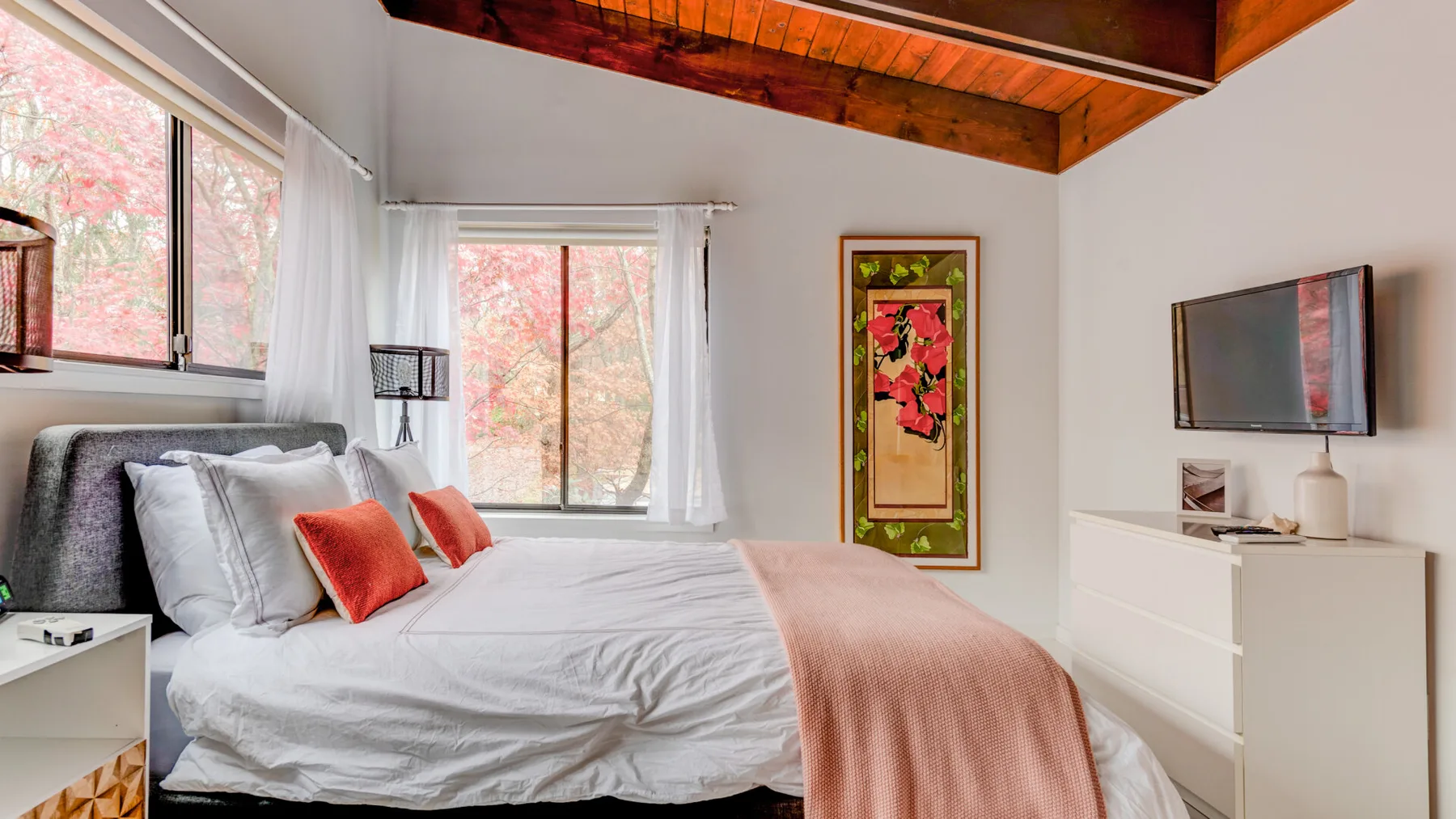 Un dormitorio luminoso con cama, ventanas grandes y un televisor montado en la pared.