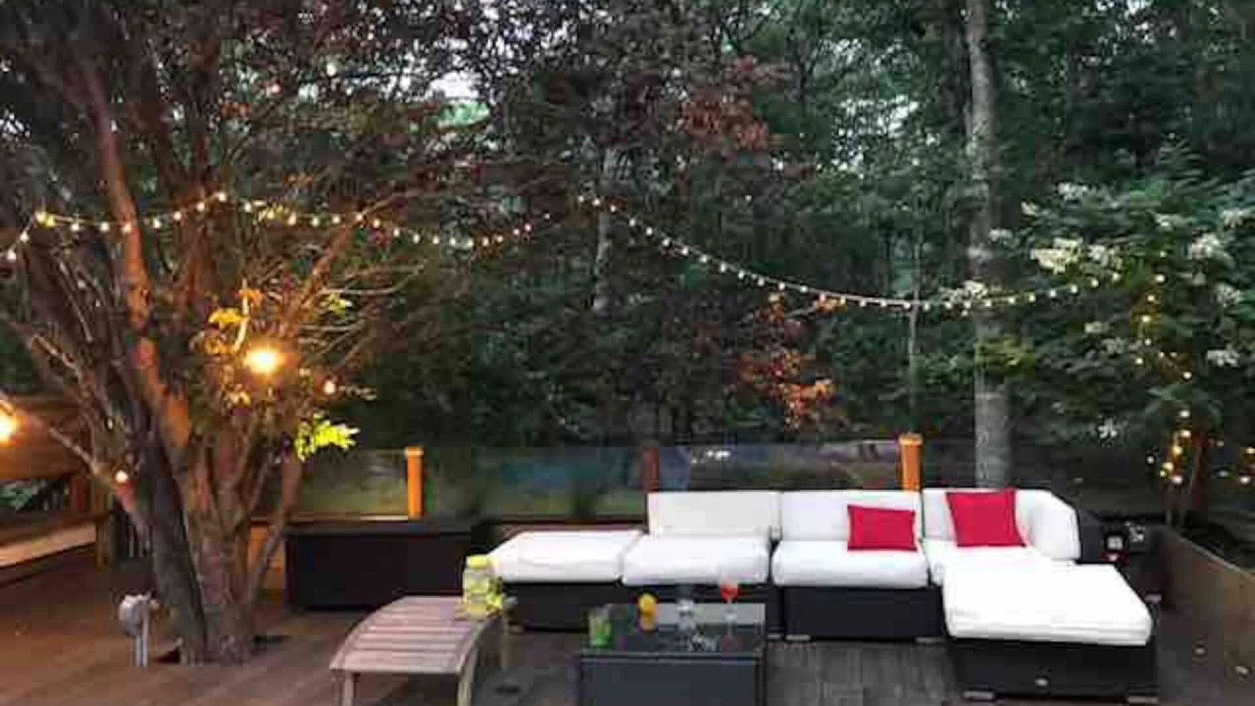 Una zona de asientos al aire libre con luces colgantes entre los árboles.