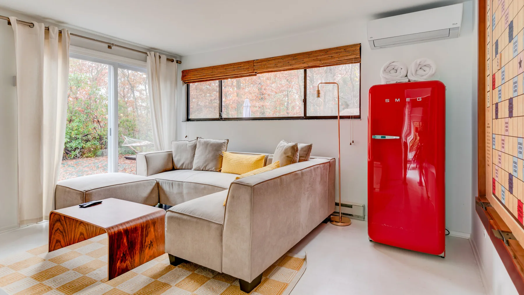 Una sala luminosa con asientos seccionales junto a grandes ventanas y un refrigerador rojo.