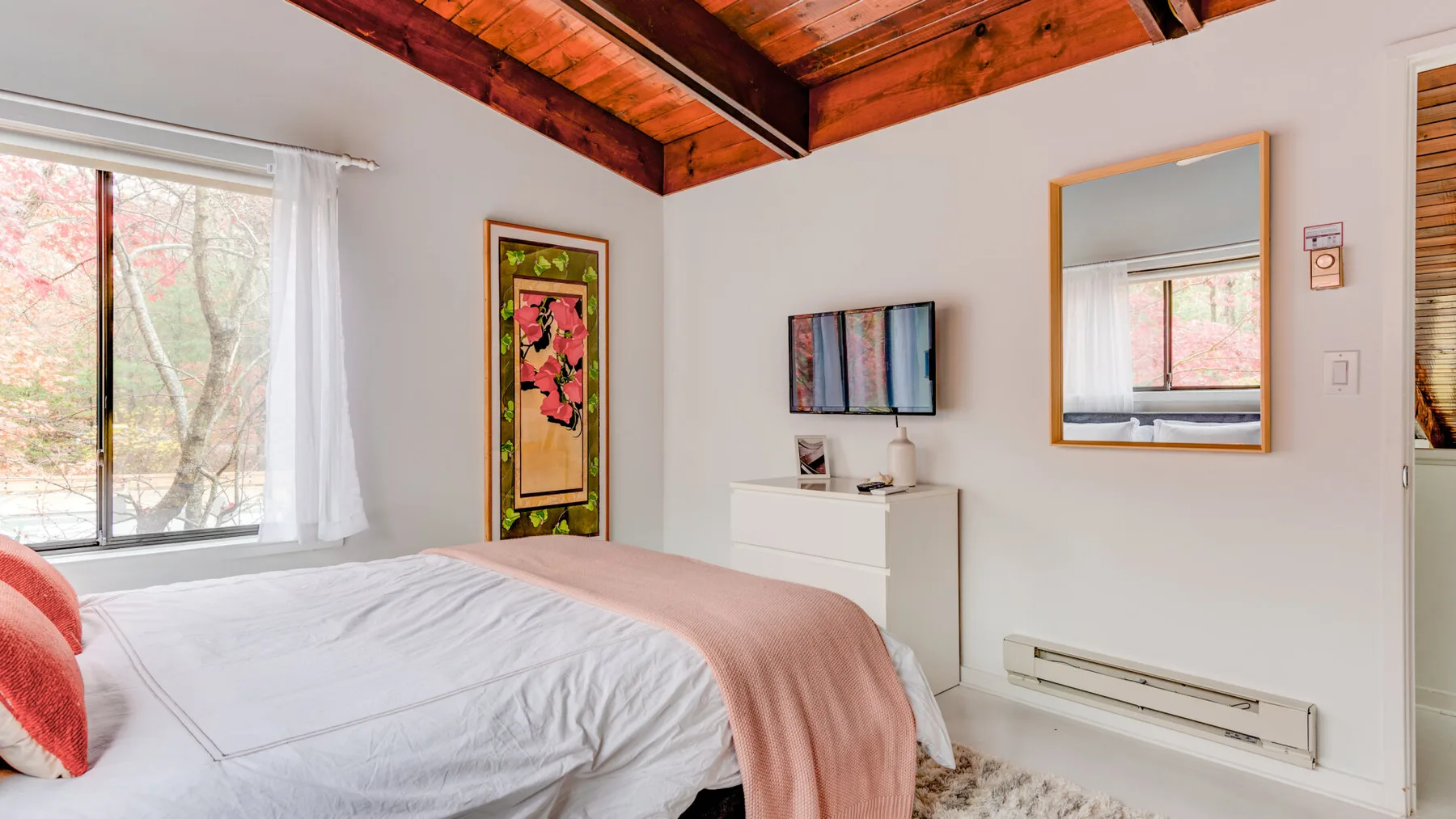 Un dormitorio con una cama, paredes blancas y vigas de madera a la vista.