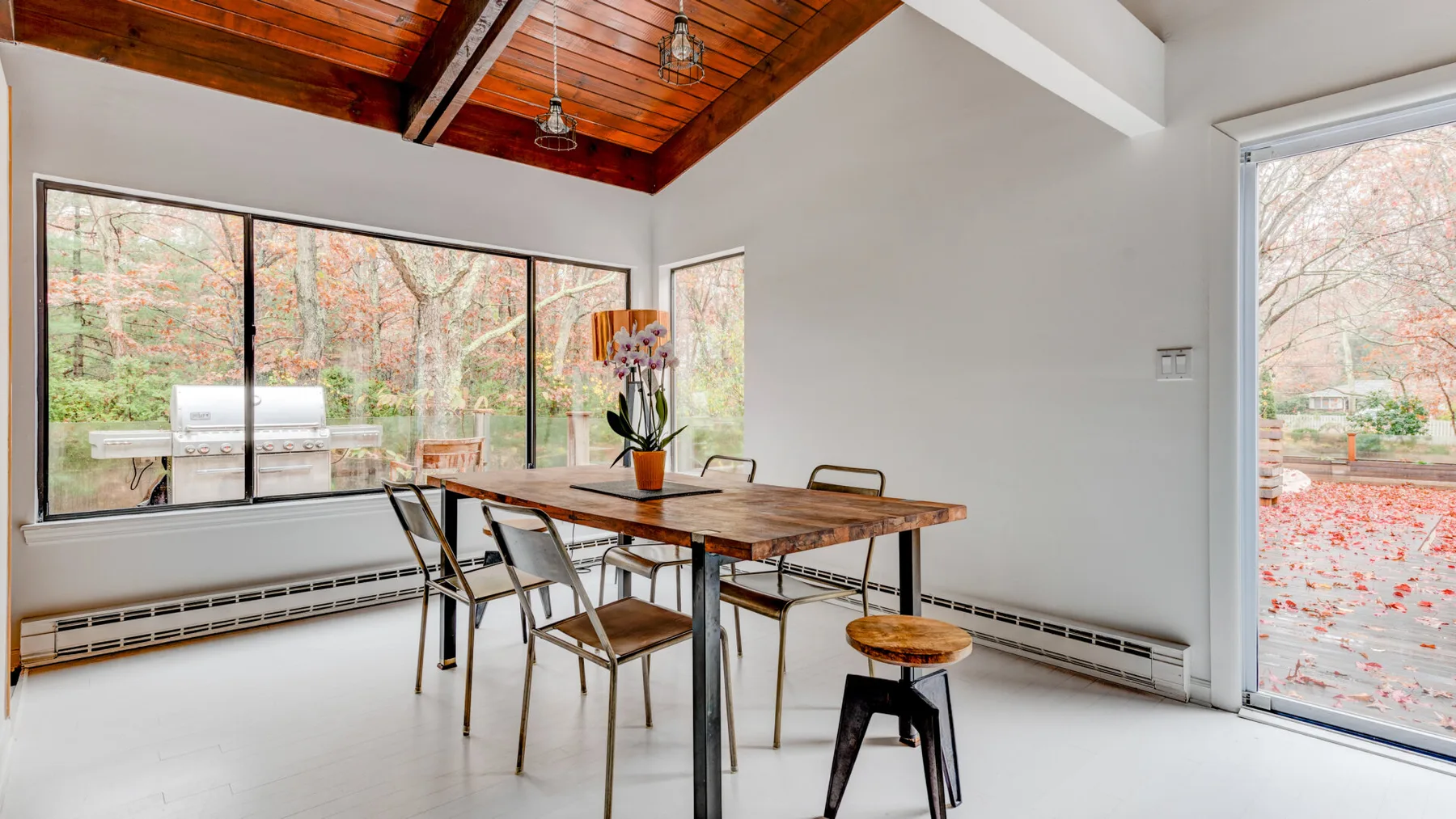 Comedor con una mesa de madera y grandes ventanas con vistas a los árboles.