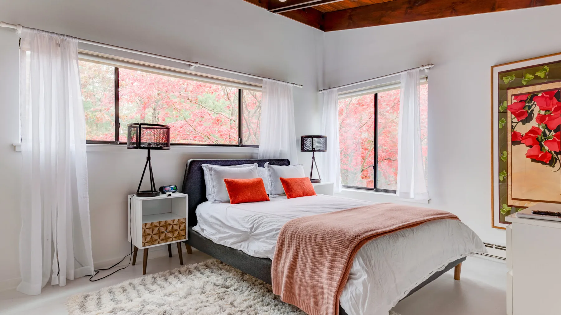 Un dormitorio luminoso con una cama junto a grandes ventanas y cortinas blancas.