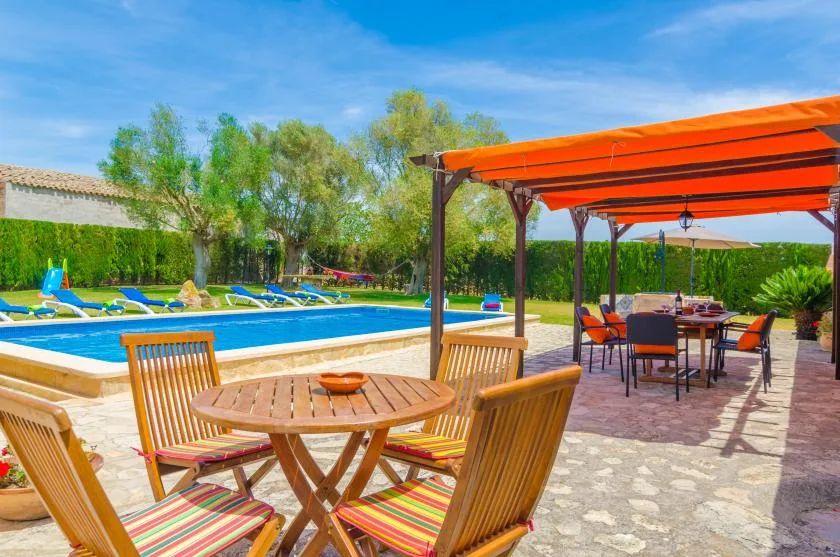 Patio junto a una piscina, con asientos de madera bajo un toldo naranja.