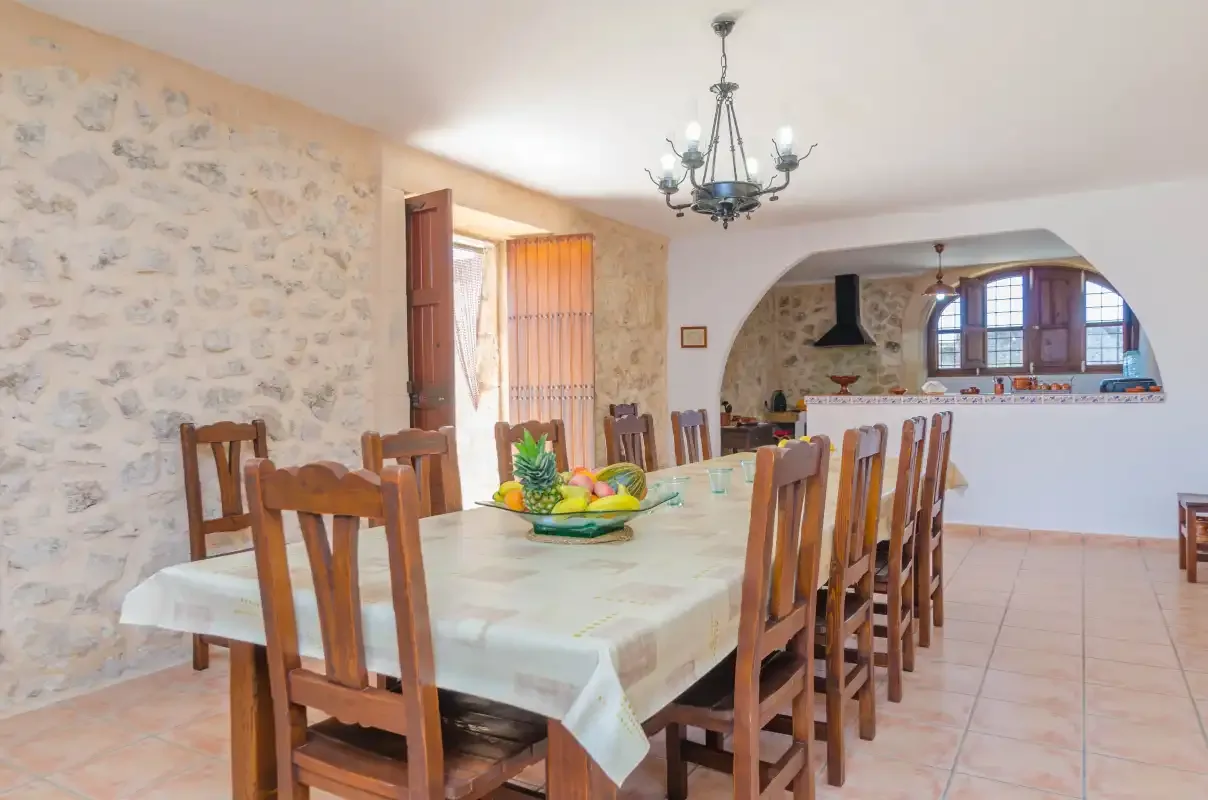 Un comedor con una mesa larga y asientos de madera junto a una abertura arqueada hacia la cocina.