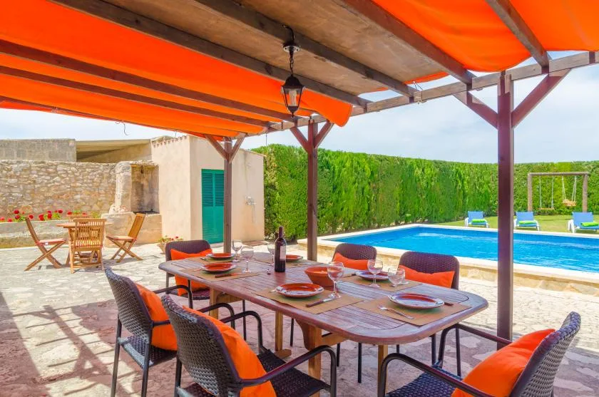 A shaded outdoor dining area overlooks a swimming pool and garden.