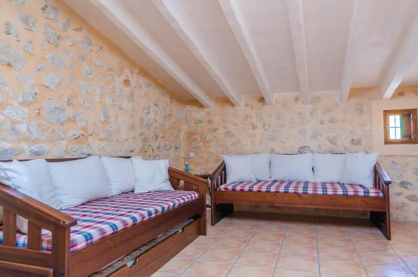 Una sala de estar rústica con asientos de madera y cojines estampados bajo vigas vistas.
