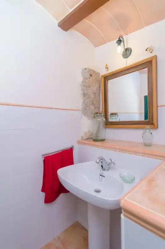 Un baño con lavabo de pedestal, espejo de pared y toalla roja.